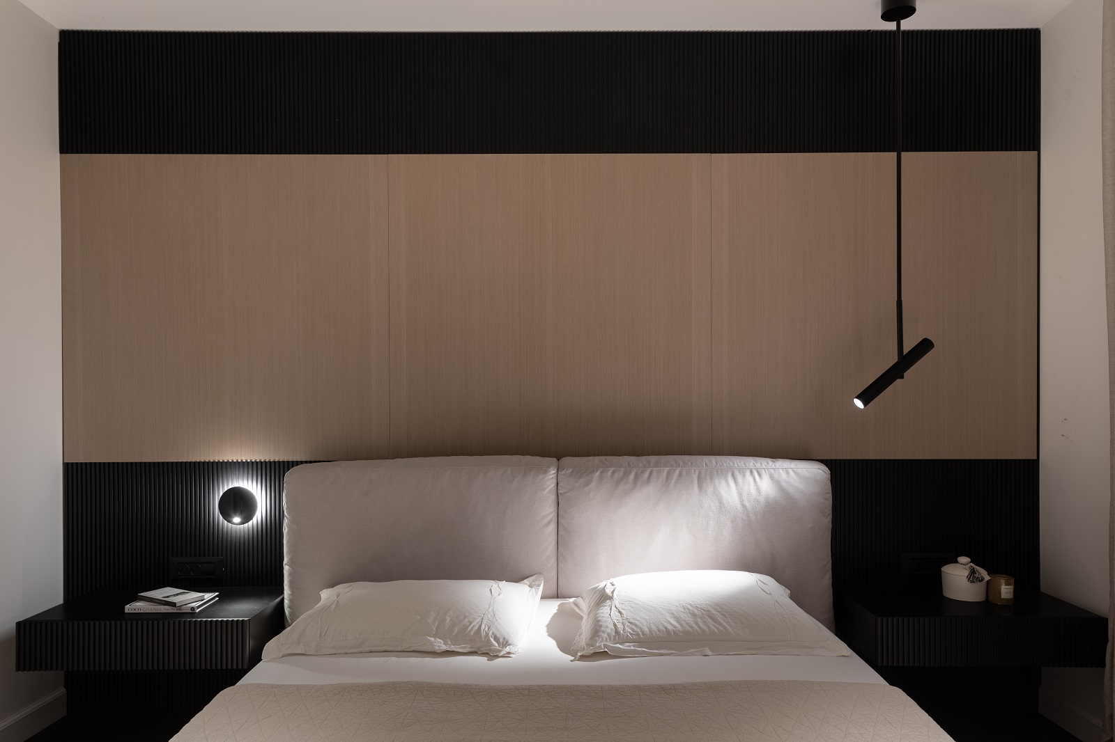 חדר שינה עם חיפוי נגרות בעץ בהיר ושני גופי תאורה דקורטיביים א-סימטריים